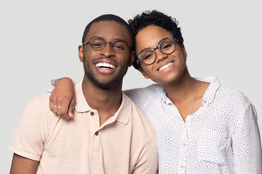 Head shot portrait African attractive married couple in glasses embracing smiling looking at camera posing isolated on grey background, love and relations, clients of photo shooting in studio concept